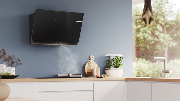 Modern kitchen with a sleek black range hood above a stovetop, emitting steam.