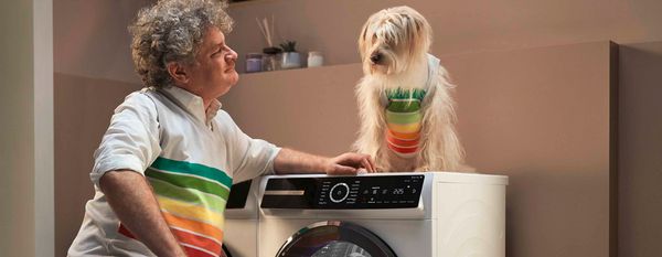 Un homme agenouillé devant un sèche-linge à pompe à chaleur Série 8, regardant son chien qui est assis sur le dessus de l'appareil. Tous deux portent un gilet avec des bandes d'efficacité énergétique.