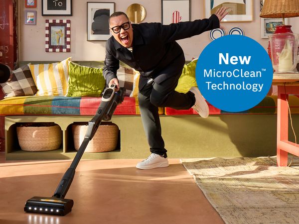 A man in formal attire vacuums a room with the Unlimited 10 vacuum cleaner, emphasizing a commitment to tidiness and style.