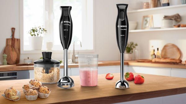 Mixeurs plongeants Bosch noirs sur un plan de travail avec fraises, smoothie, muffins et hachoir.
