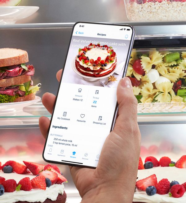 A person holding a smartphone in front of a Bosch French door fridge freezer, showcasing its features and design.