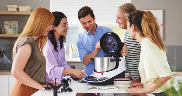 Gruppe von Menschen schaut gespannt auf ein Cookit während einer Präsentation in einer Küche.