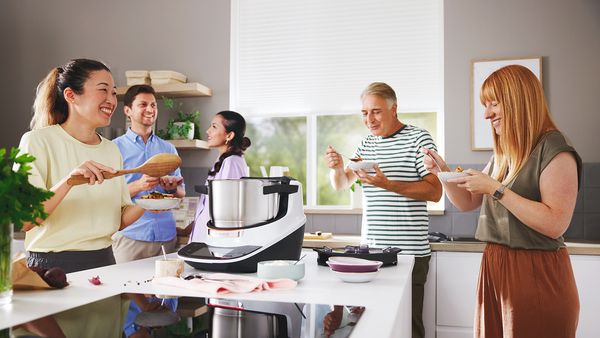Menschen probieren Essen, das mit einem Cookit zubereitet wurde, in einer freundlichen Küchenumgebung.