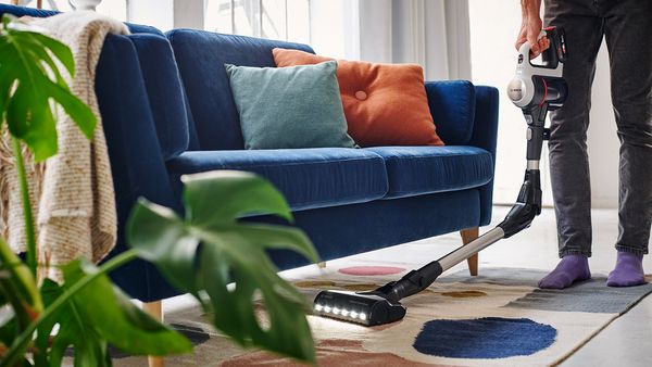 Eine Person staubsaugt einen weißen Wohnzimmerteppich auf dem sich viele Krümel befinden mit dem Bosch Unlimited 10 Akku-Staubsauger.