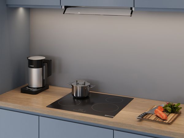Piano cottura elettrico Bosch con pentola in acciaio, bollitore elettrico e tagliere con verdure su top cucina in legno