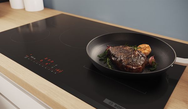 Table de cuisson aspirante avec une casserole et une poêle dont les fumées sont aspirées