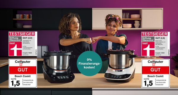 Zwei Frauen stoßen in einer Küche mit Fäusten an, während zwei Bosch Cookit Küchenmaschinen auf der Arbeitsplatte kochen. Ein Testsiegel zeigt die Bewertung „GUT (2,0)“ von Stiftung Warentest, und ein lila Hinweis weist auf 0% Finanzierung hin.