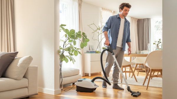 Ein Mann staubsaugt den Hartboden einer modernen, hellen Wohnung mit einem Bosch Staubsauger mit HEPA-Filter.