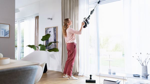 Eine Frau reinigt Fensterrahmen mit einem Unlimited 7 Akku-Staubsauger.