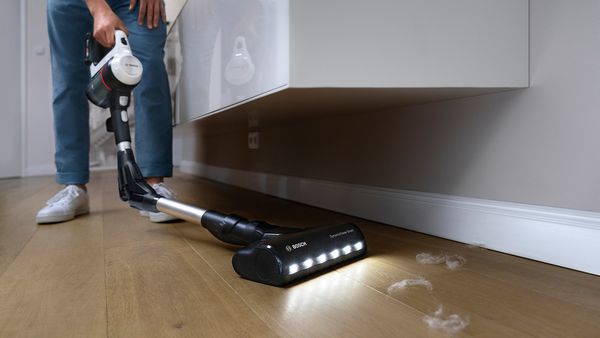 Eine Person saugt mit dem Unlimited 7 Akku-Staubsauger unter einem Lowboard.