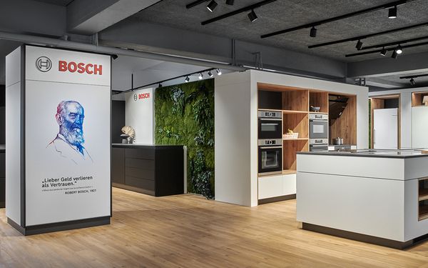 Moderner Bosch-Showroom mit Küchengeräten und grüner Wand auf Holzboden.