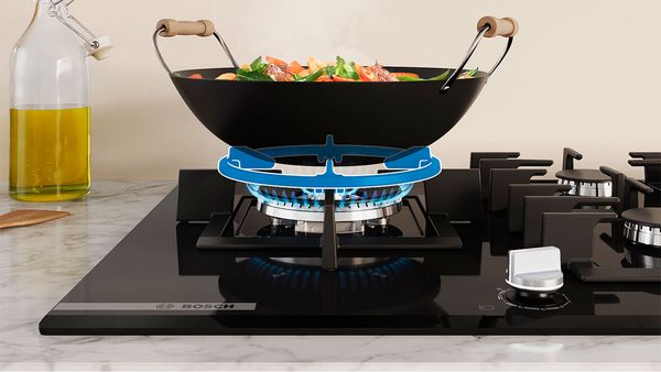 Un wok noir avec légumes colorés en cuisson sur une plaque gaz Bosch moderne.