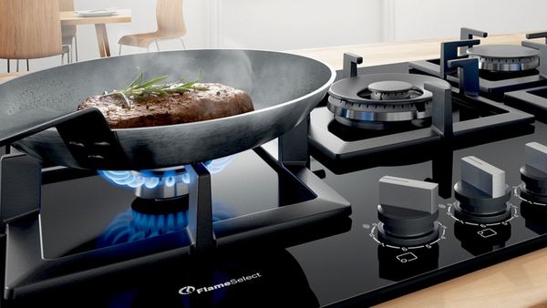 A stove top featuring FlameSelect and a single pan resting cooking a steak.
