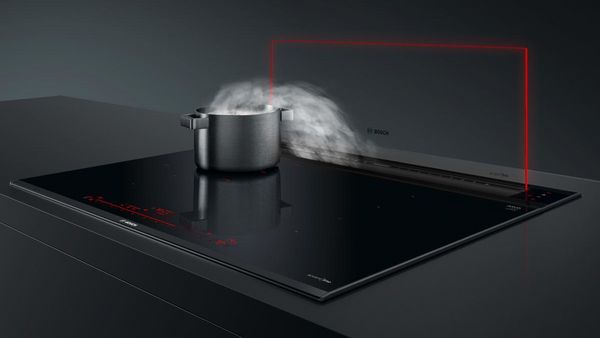 Casserole d&eacute;gageant de la vapeur sur une plaque &agrave; induction noire avec hotte plan de travail Bosch.