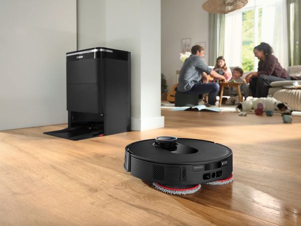 Spotless friega el suelo de madera mientras la familia se relaja en el salón al fondo.