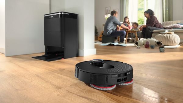 Bosch robotski usisavač i čistač podova na parketu u obiteljskom stanu, u pozadini obitelj provodi zajedničko vrijeme.