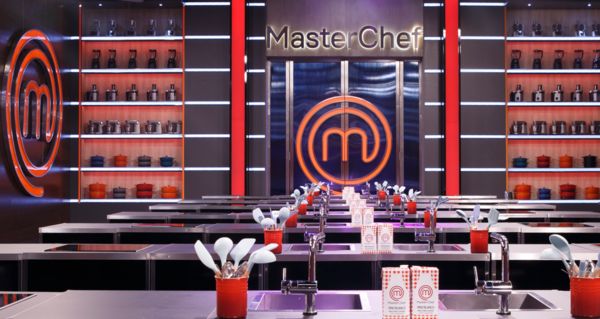 Moderno juego de cocina MasterChef, con letreros de color naranja vibrante, elegantes estaciones de cocina y utensilios e ingredientes bien ordenados.