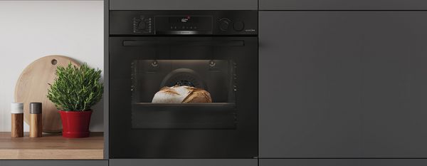 Een lichte, moderne keuken met een pan en een koekenpan op het fornuis en twee ovens op de achtergrond.