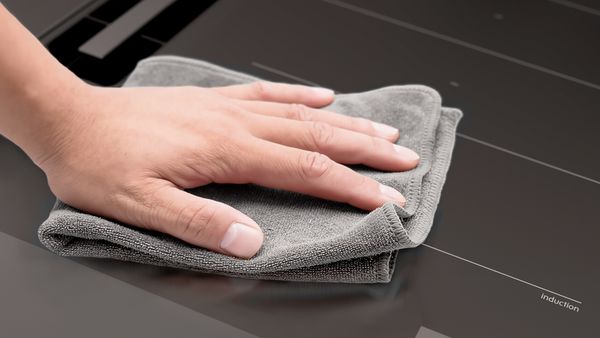 Hand reinigt inductiekookplaat met grijze microvezeldoek