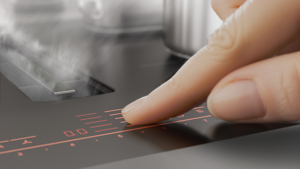 Bedienung des Kochfelds über das Touchdisplay mit Finger in Nahaufnahme.
