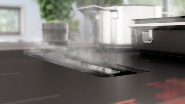 Close-up van de matte kookplaat met afzuiging waardoor je goed ziet dat de stoom verdwijnt in het ventilatierooster