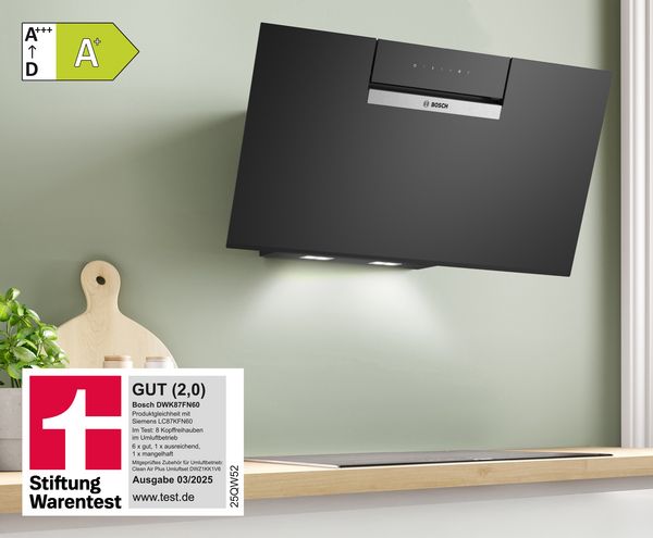 Schwarze BOSCH Kopffreihaube in einer Küche, mit einem Bewertungsiegel der Stiftung Warentest für die Note GUT, daneben ein Holzschneidebrett.