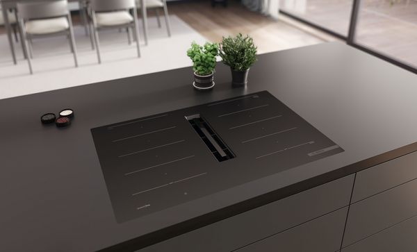 Modern keukenblad met geïntegreerde zwarte kookplaat en strak design, omringd door klein potplantje.