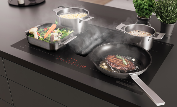 Vue lat&eacute;rale en plong&eacute;e de la table de cuisson aspirante Bosch Series 6 avec zones XL Flex. 2 ustensiles de cuisson remplis de chaque c&ocirc;t&eacute; de la table.