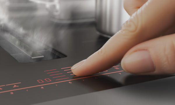 Gros plan du panneau de commande tactile de la table de cuisson aspirante Series 8 au design mat noir carbone ; un doigt appuie dessus.