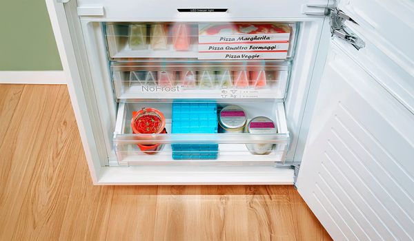 Un cong&eacute;lateur bien organis&eacute; contenant des pizzas, des bocaux et des contenants de gelato sur des &eacute;tag&egrave;res transparentes.