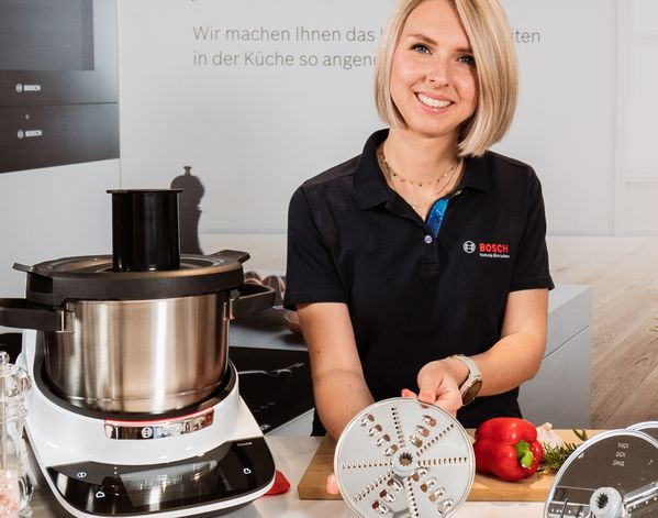 Eine Küchenausstellung mit Bosch-Geräten, darunter Mixer und Kochutensilien, zusammen mit frischen Kräutern und Gemüse auf einer Arbeitsplatte.