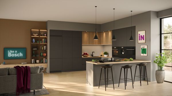 Cocina moderna con armarios oscuros, detalles de madera, lámparas colgantes negras, una elegante isla y una acogedora zona de estar decorada.