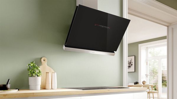 Modern kitchen featuring a sleek black and stainless steel range hood above a wooden countertop, with green walls and decorative kitchen items.