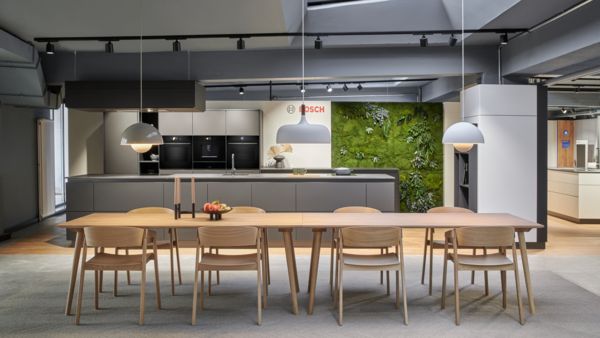 Moderner Bosch Showroom mit eleganten Haushaltsgeräten, Esstisch aus Holz und einer bepflanzten Wand für ein frisches Ambiente.