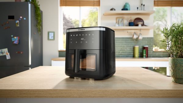 Two Bosch Air Fryer model  Serie 6, placed side by side on a kitchen island, with plates of vegetarian and meat dishes arranged around them.