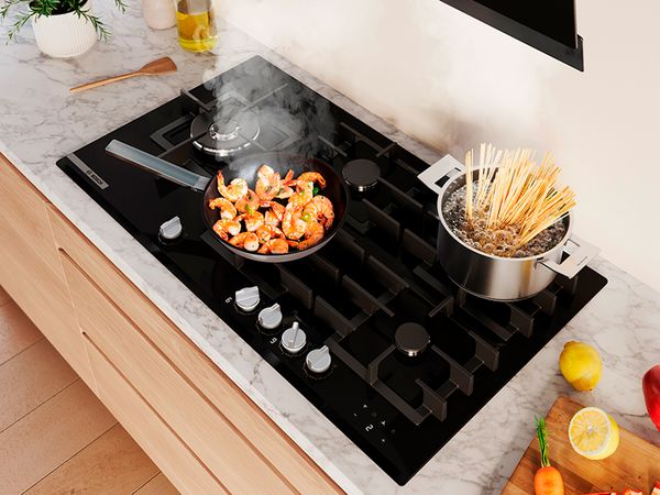 Piano cottura a gas Bosch con padella di gamberi in cottura e pentola con spaghetti in ebollizione