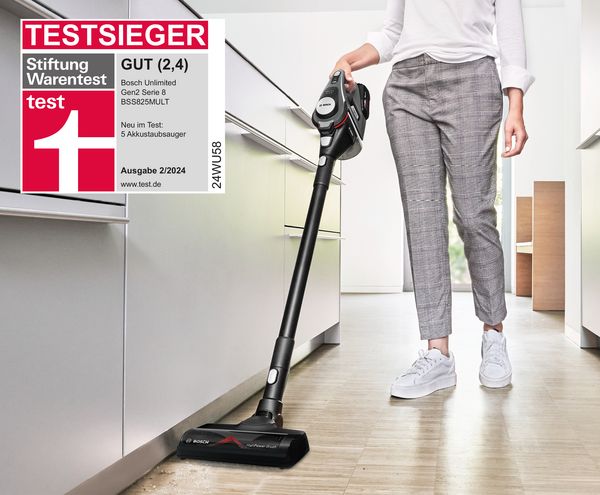 Eine Frau saugt in einer modernen Küche mit einem schwarzen Bosch Serie 8 beutelloser Staubsauger BSS825MULT, der von der Stiftung Warentest als Testsieger und mit der Note "Gut" bewertet wurde.