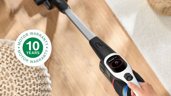 Cordless vacuum Unlimited 9 cleaning on hard floor, next to it a seat cushion and the logo for 10 years motor warranty.