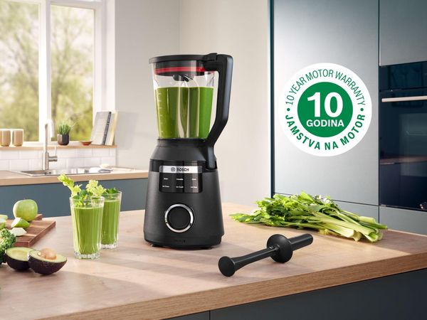 Elegantan crni blender sa zelenim smoothiejem na pultu, uz svježe sastojke i jamstvo motora od 10 godina. 