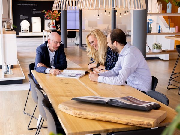 drie mensen aan een tafel praten en kijken naar magazine