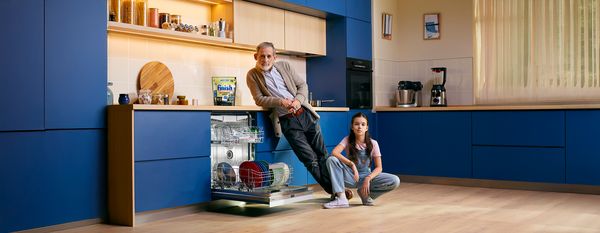 Twee personen laden vaatwasser met kleurrijke borden en borden.