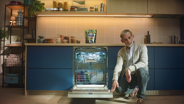 Person kneeling next to open dishwasher with Finish pack on top