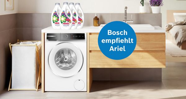 Eine moderne Waschküche mit einer Bosch-Waschmaschine, einem Wäschekorb und Ariel-Waschmittelflaschen, die das Engagement von Bosch für Ariel unterstreichen.