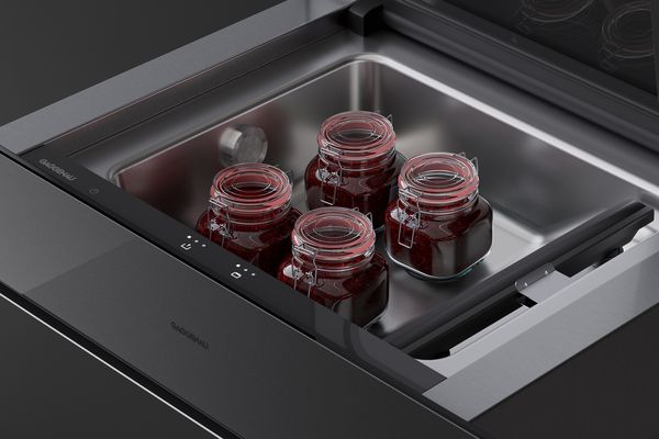 Зображення вакуумної шухляди мінімалістичної серії Gaggenau крупним планом, показано відкритою з банками фруктових консервів