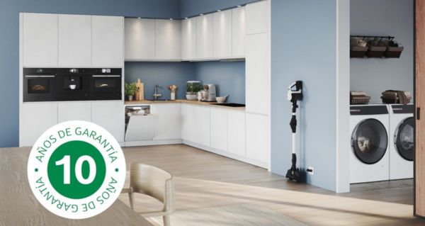 Un distintivo de garantía de 10 años superpuesto a una imagen de una cocina moderna y luminosa con horno, aspiradora, lavadora y lavavajillas integrados.