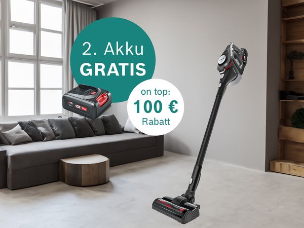 Ein stilvolles Wohnzimmer mit einem Staubsauger und einem Werbeschild mit der Aufschrift „2. Akku GRATIS“ und „100€ Rabatt“ neben einem kostenlosen Akkupack.