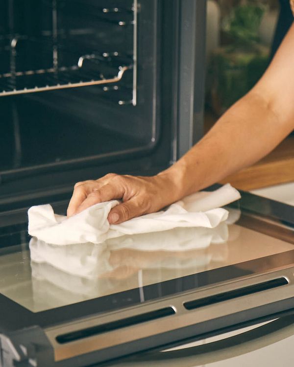 Mano che pulisce con un panno il vetro del forno aperto