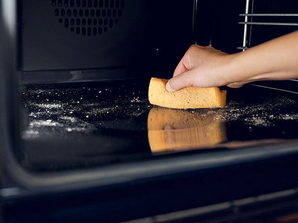 Mano che pulisce il fondo del forno con una spugna 