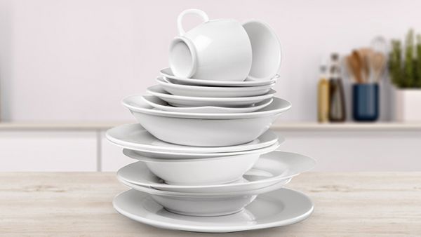 Torre de diversas piezas blancas de cerámica, platos, tazones y tazas sobre una mesa de madera. 