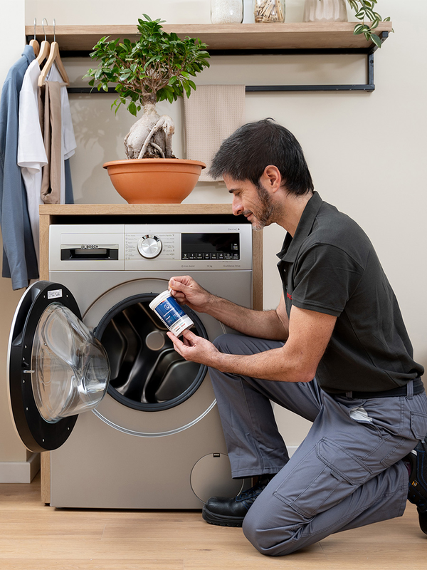 Un technicien tenant un produit d'entretien devant un lave‑linge.